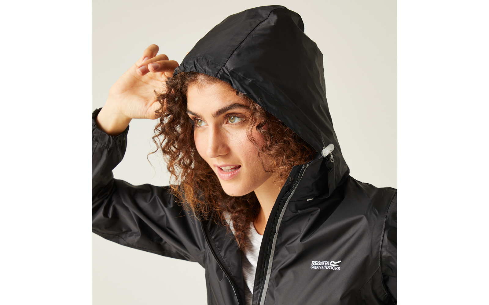 Persona con capelli ricci tira su il cappuccio di una giacca antipioggia nera, logo visibile sul petto