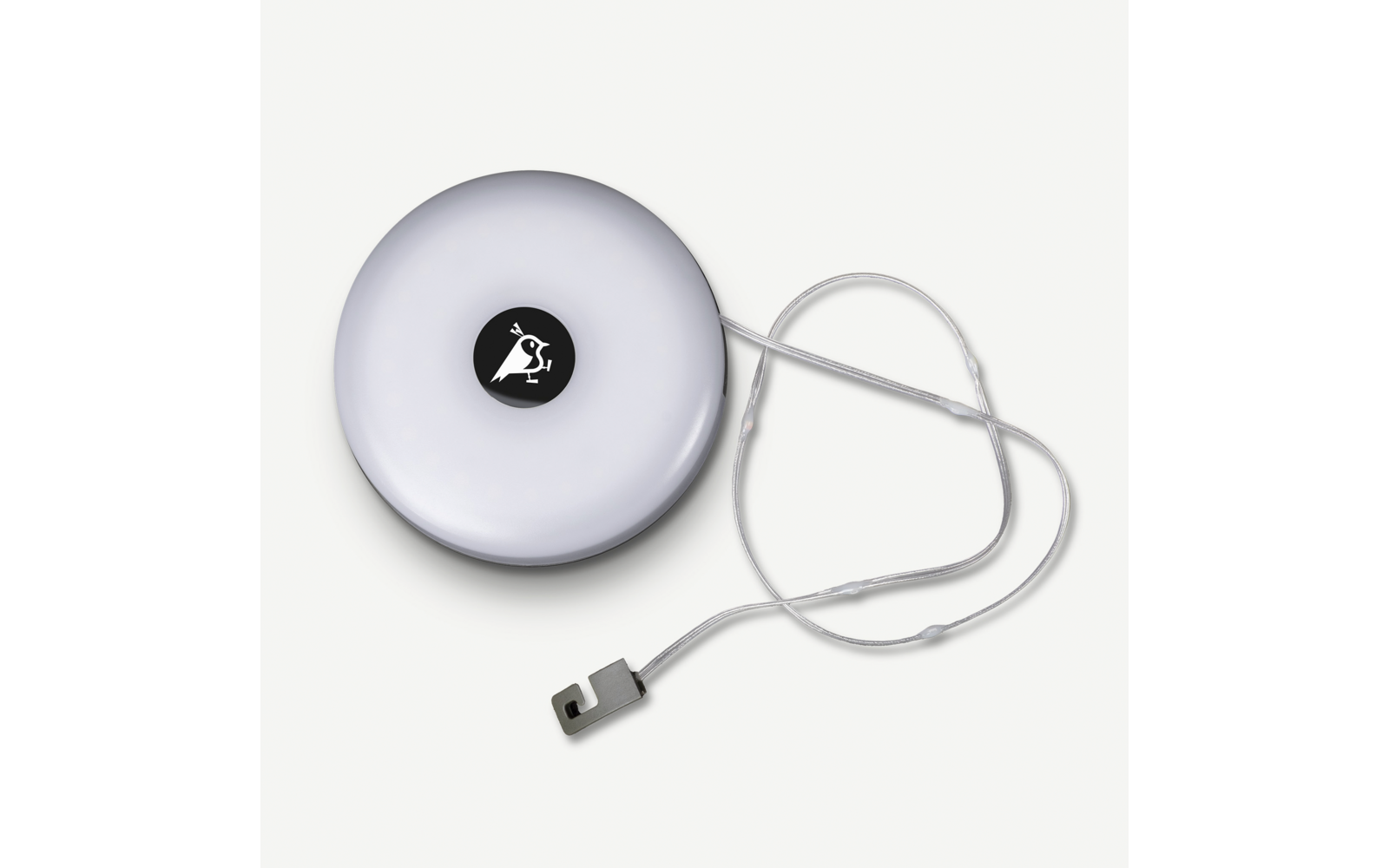 Rundes weißes Gehäuse mit schwarzem Kreis und weißem Symbol in der Mitte, aufgerolltes transparentes Band mit Metallhaken neben dem Gehäuse, heller Hintergrund