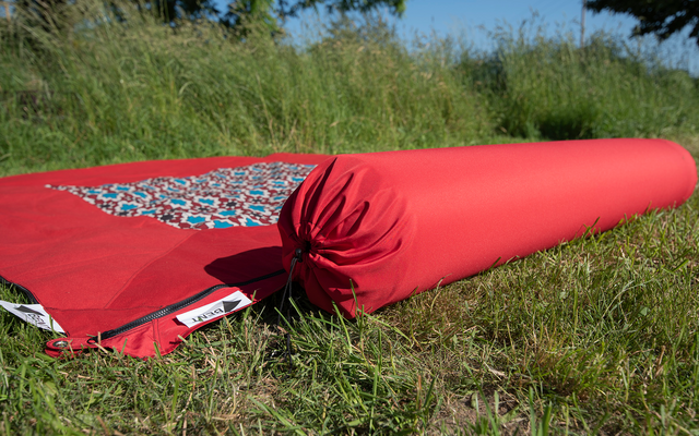 Red rolled-up yoga mat lying on grass