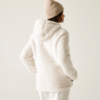 Frau von hinten mit weißer, kapuzenbekleideter Teddyjacke und beiger Mütze