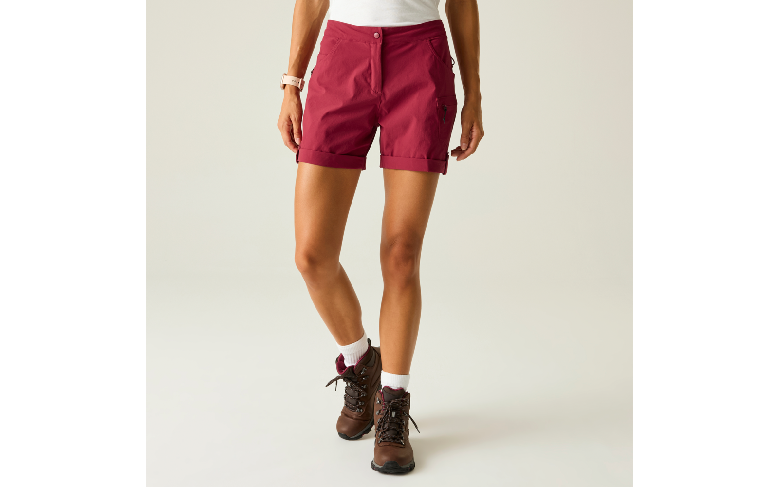 Unterkörper einer stehenden Person mit bordeauxroten Shorts, weißem Oberteilsaum, weißen Socken und braunen knöchelhohen Schuhen vor hellem Hintergrund