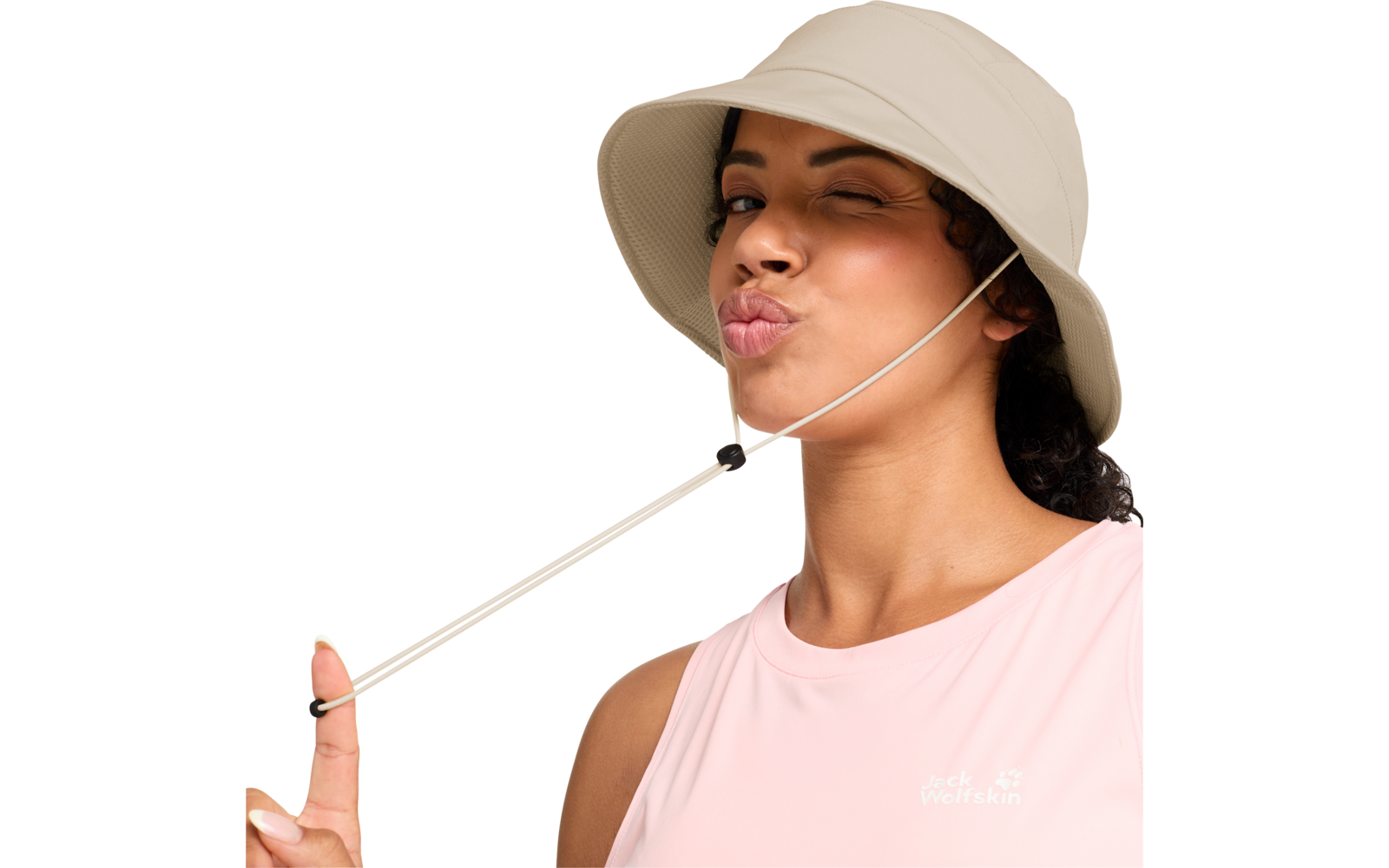Person mit beigem Anglerhut zwinkert, macht einen Kussmund, hält den Hutriemen und trägt ein hellrosa ärmelloses Oberteil