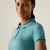 Person, Brustansicht, leichter Lächeln, trägt türkisfarbenes Poloshirt mit kleinen Logos auf Brust und Ärmel, Zöpfe nach hinten gelegt, einfarbiger heller Hintergrund