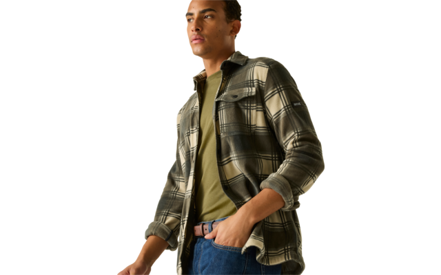 Persoon draagt groen-zwart geruit overshirt, olijfgroen T-shirt en blauwe spijkerbroek, hand in zak, kijkt naar rechts