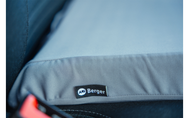 Gray padded cushion with black fabric label "Berger", on a dark textured surface; red plastic piece at bottom left