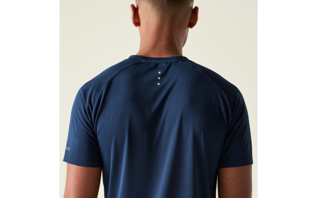 Rückenansicht einer Person mit kurzem Haar, dunkelblaues kurzärmeliges T-Shirt mit drei kleinen weißen Punkten auf dem oberen Rücken, heller beiger Hintergrund