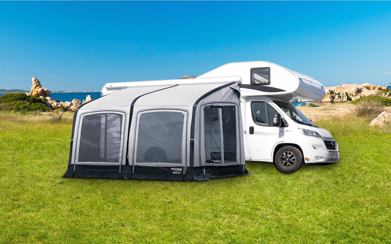 Wohnmobil mit angebautem grau-weißem Vorzelt auf grüner Wiese bei blauem Himmel
