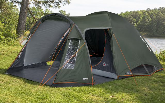 Groene tent met twee compartimenten, open ingang, oranje scheerlijnen, op gras bij een meer, bomen op de achtergrond