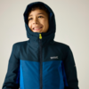 Enfant souriant portant une veste bleue à capuche, regardant vers le haut, fond clair, logo visible sur la poitrine