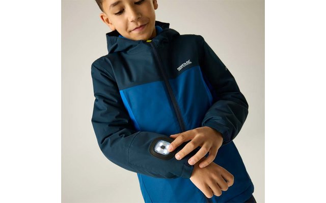 Un garçon en veste à capuche bleue touche une lampe ronde sur son avant-bras gauche