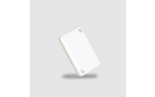 Weißes rechteckiges Kunststoffplättchen mit abgerundeten Ecken und zwei dreieckigen Aussparungen in den Ecken, schräg angeordnet, Schatten auf hellgrauem Hintergrund