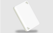 Piastrina rettangolare in plastica bianca con angoli arrotondati e due ritagli triangolari negli angoli, inclinata, ombra su sfondo grigio chiaro