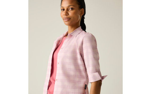 Person mit zurückgebundenem Zopf, trägt hellrosa karierte Jacke über rosa Oberteil, vor hellem einfarbigem Hintergrund