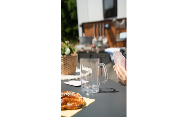 Glas, Kaffeetasse und Croissant auf einem Tisch, im Hintergrund Küchenregal mit Geschirr