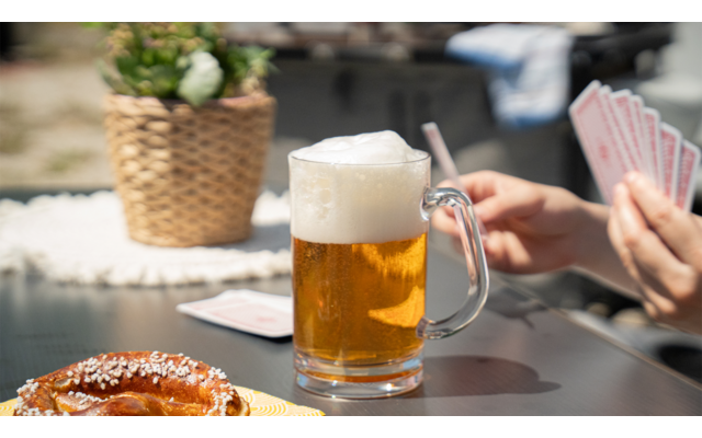 Hand hält Gabel über Teller mit Essen neben Glas Bier auf Tisch