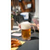 Glas Bier mit Schaum auf einem Tisch, unscharfer Hintergrund mit Gästen