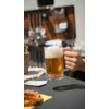 Hand hält ein Glas Bier in einem hellen Café, Tische mit Speisen und Getränken im Hintergrund