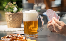 Glas Bier mit Schaum, Hände halten Spielkarten, Brezel auf Tisch