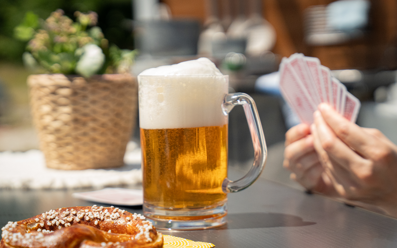 Glas Bier mit Schaum, Hände halten Spielkarten, Brezel auf Tisch