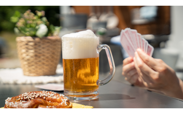Glas Bier mit Schaum, Hände halten Spielkarten, Brezel auf Tisch