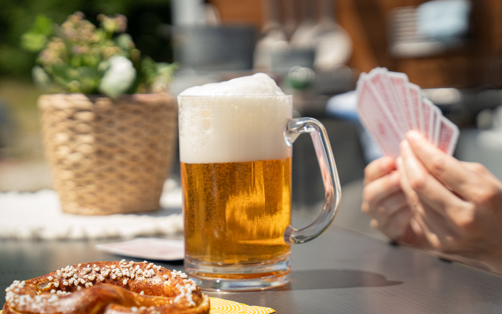 Glas Bier mit Schaum, Hände halten Spielkarten, Brezel auf Tisch