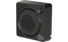 Schwarzes quadratisches Gehäuse mit abgerundeten Ecken, großer kreisförmiger vertiefter Bereich mit schräg angeordneten Schlitzen, kleine runde Öffnung oben rechts, weißes Haus‑Signal‑Icon unten rechts