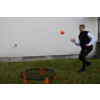 Mann wirft einen Ball auf ein rundes Netzspiel im Freien vor einer weißen Wand