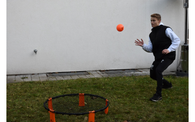 Mann wirft einen Ball auf ein rundes Netzspiel im Freien vor einer weißen Wand