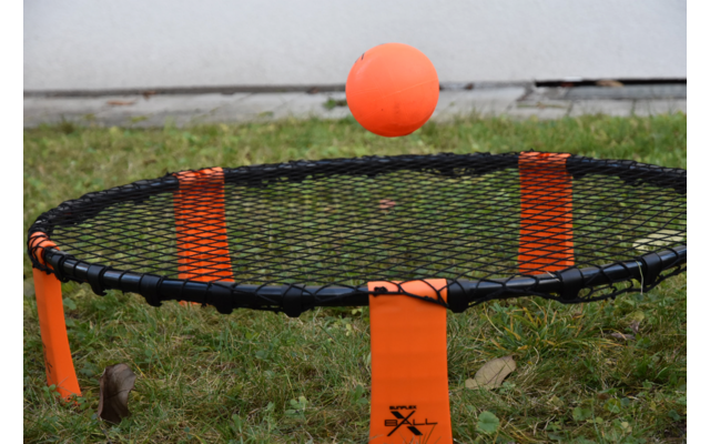 Ein orangefarbener Ball über einem schwarzen und orangen Rundnetz auf Grasboden