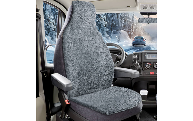 Fahrersitz mit grauem, flauschigem Sitzbezug, Lenkrad und Armaturenbrett; Pappbecher im Getränkehalter; durch die Windschutzscheibe schneebedeckte Bäume und ein fahrendes Auto auf einer verschneiten Straße