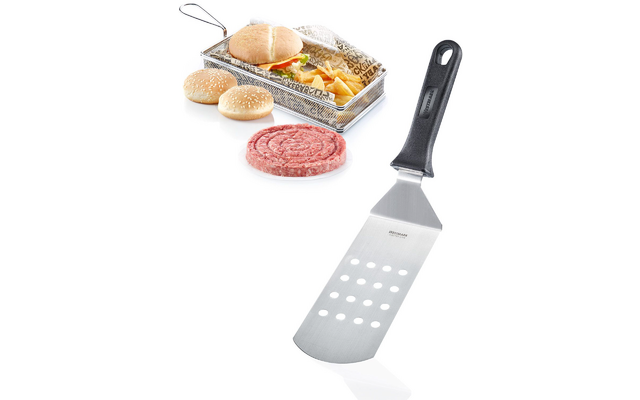 Espátula de acero inoxidable con mango negro en primer plano; al fondo dos panes con sésamo, una hamburguesa cruda de forma redonda en un plato blanco y una hamburguesa montada con patatas fritas en una cesta metálica