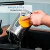 Hand with sponge cleaning a stainless steel kettle over a sink, water pouring from the spout; visible label reading 'KINDERLEICHTE REINIGUNG'