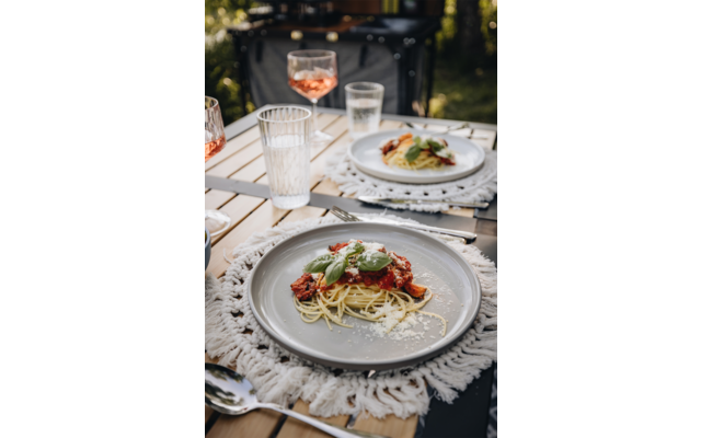 Ein gedeckter Tisch im Freien mit einem Teller Essen, Glas Wasser und Besteck