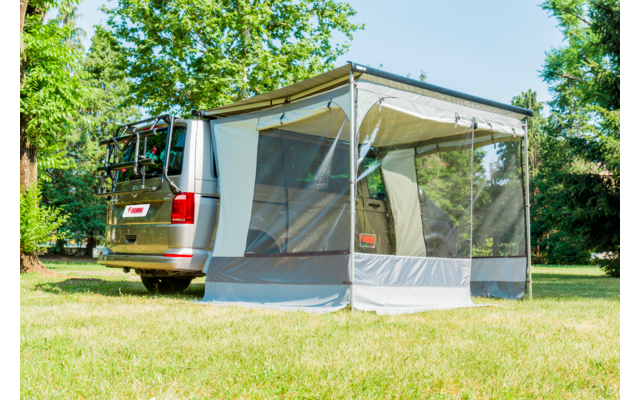 Camper argentato con tenda annessa grigio-bianca con pannelli a zanzariera, parcheggiato sull'erba davanti ad alberi