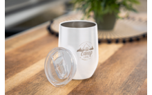 Weißer Edelstahlbecher mit Deckel auf Holztisch, Aufschrift 'Camp Life' und Bergmotiv