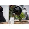 Zwarte waterkoker giet heet water in een wit glas met deksel, plant en stoel op houten tafel op de achtergrond
