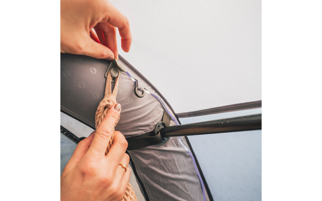 Zwei Hände befestigen ein Seil an einer Öse des Zeltdachs neben einer Zeltstange