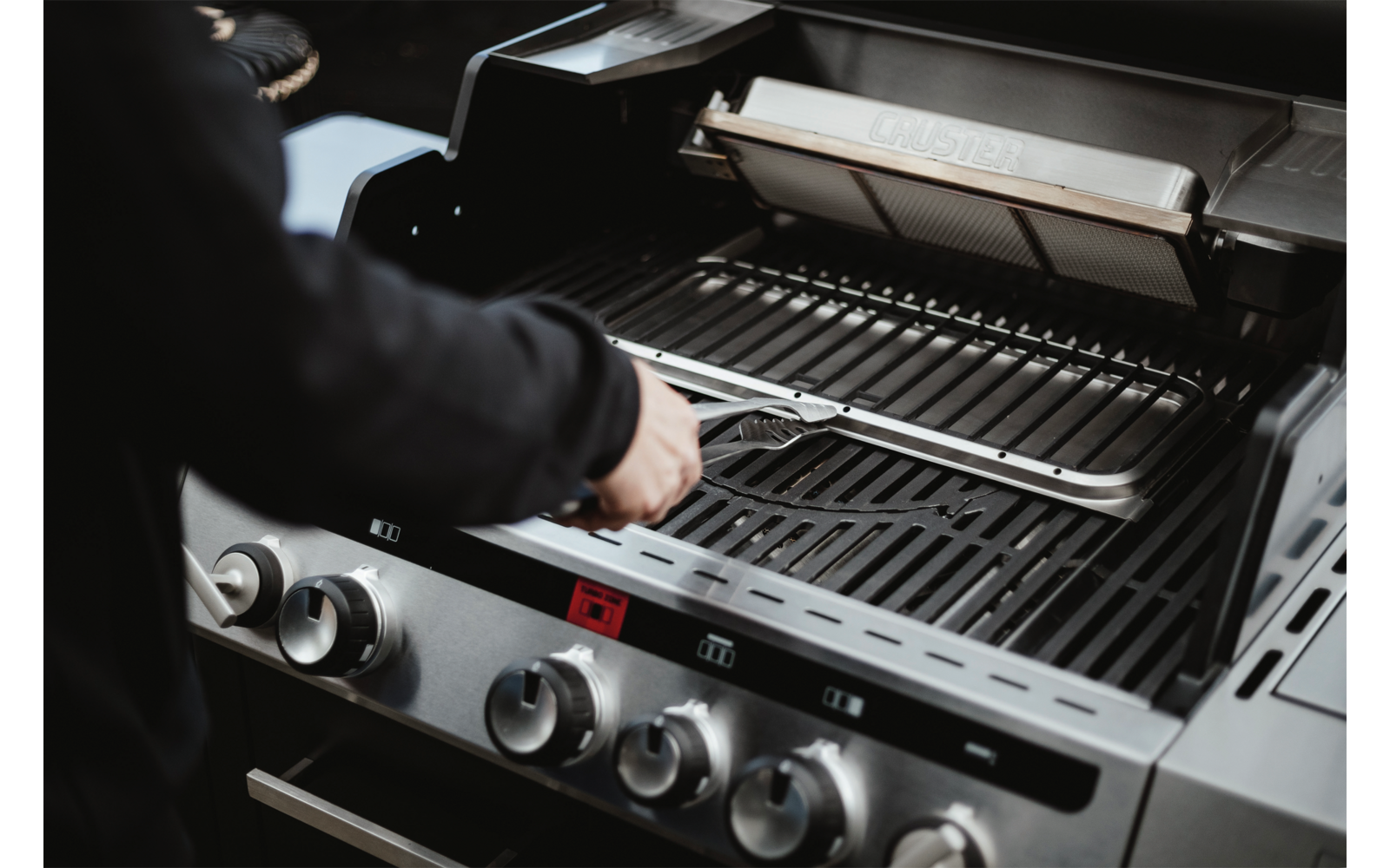 Hand öffnet den Deckel eines Gasgrills mit sichtbaren Grillrosten