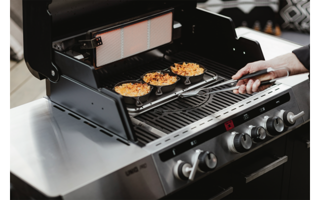 Ein Gasgrill mit mehreren Burger-Patties auf dem Rost und einer Hand, die eine Grillzange hält