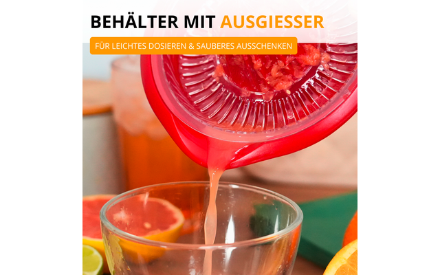 Récipient plastique rouge avec bec verseur versant un liquide rose-orangé dans un verre ; pamplemousse coupé en deux et tranches de fruits au premier plan, main tenant le récipient