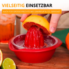 Main pressant un agrume coupé en deux à la pulpe rouge sur une presse à jus rouge ; le jus coule dans la coupelle, quartier de citron vert, orange et verre avec boisson sur une surface en bois en arrière‑plan