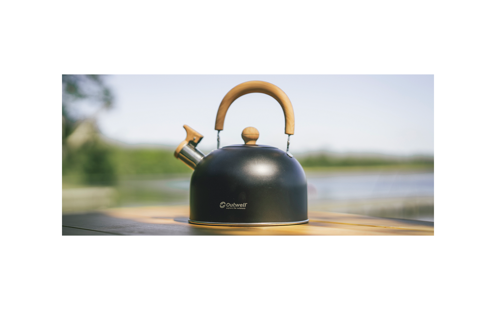 Zwarte theeketel met houten handvat op houten oppervlakte, wazige achtergrond met lucht en water