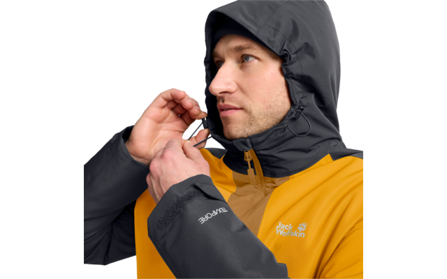 Person mit dunkelgrauer Kapuze zieht an der Kordel einer gelben Jacke, Jack Wolfskin-Logo auf Brust und Ärmel sichtbar