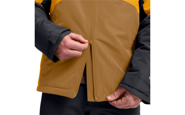 Hände, die an einem Reißverschluss einer zweifarbigen Jacke (braun und gelb) mit schwarzen Ärmeln ziehen