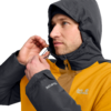 Person mit dunkelgrauer Kapuze zieht an der Kordel einer gelben Jacke, Jack Wolfskin-Logo auf Brust und Ärmel sichtbar