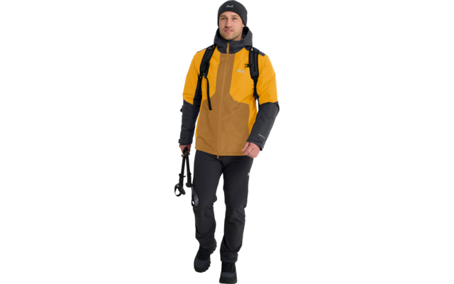Person mit gelber Jacke, schwarzer Mütze, schwarzer Hose, mit Rucksack, hält eine Kamera in der rechten Hand