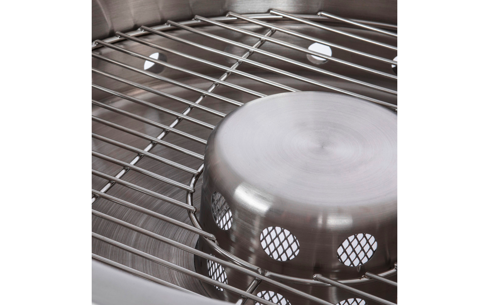 Nahaufnahme einer Edelstahloberfläche mit Drahtgitter und einer umgedrehten, gelochten Metallschale