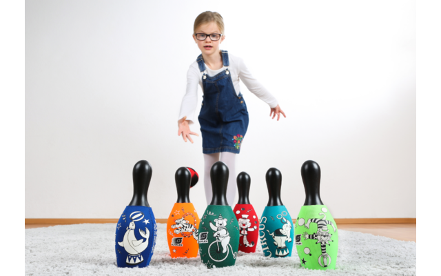 Kind steht neben sechs bunten Bowling-Pins, posiert mit erhobenem Daumen
