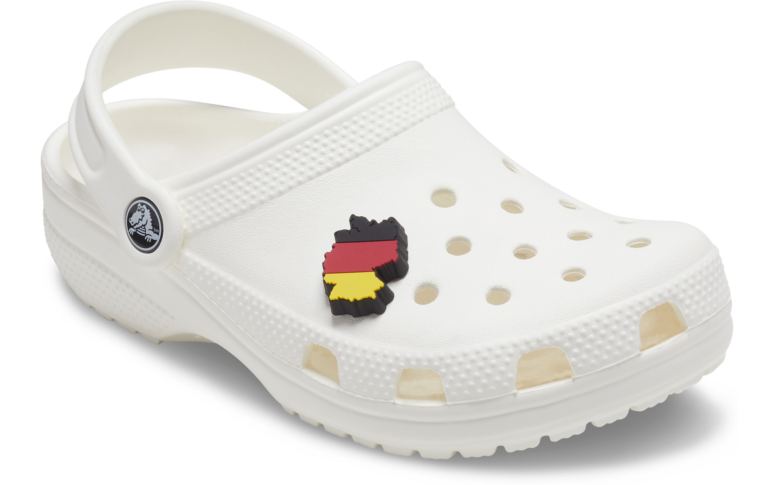 Zueco blanco con orificios de ventilación y correa en el talón, en un orificio un colgante en forma de contorno con franjas negras, rojas y amarillas