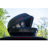 Box da tetto nero aperto sul tetto di un'auto, scritta rossa, alberi sullo sfondo